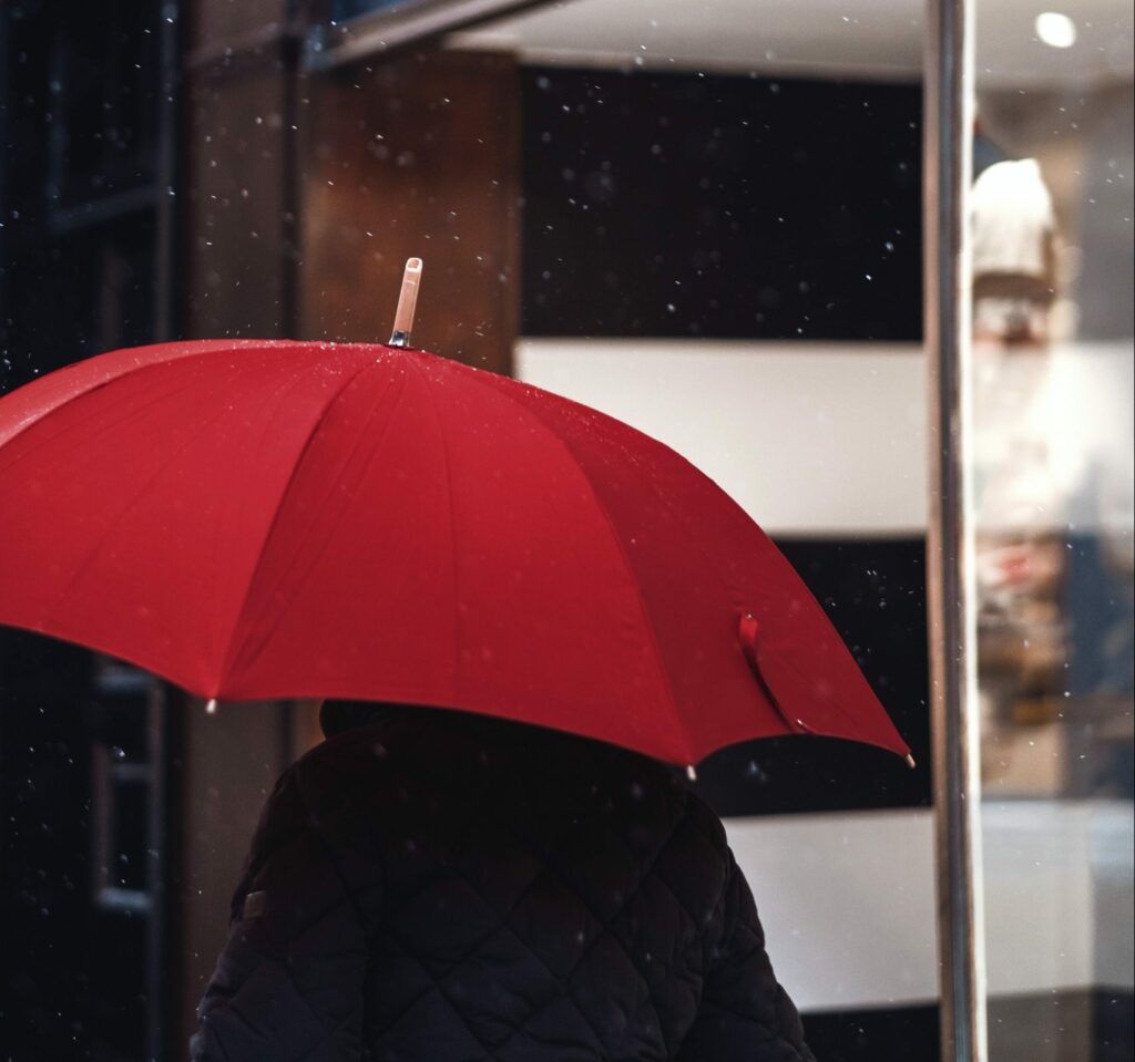 A man walks past a shop, holding a red umbrella above his head. Photo by Craig Whitehead on Unsplash