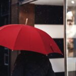 A man walks past a shop, holding a red umbrella above his head. Photo by Craig Whitehead on Unsplash