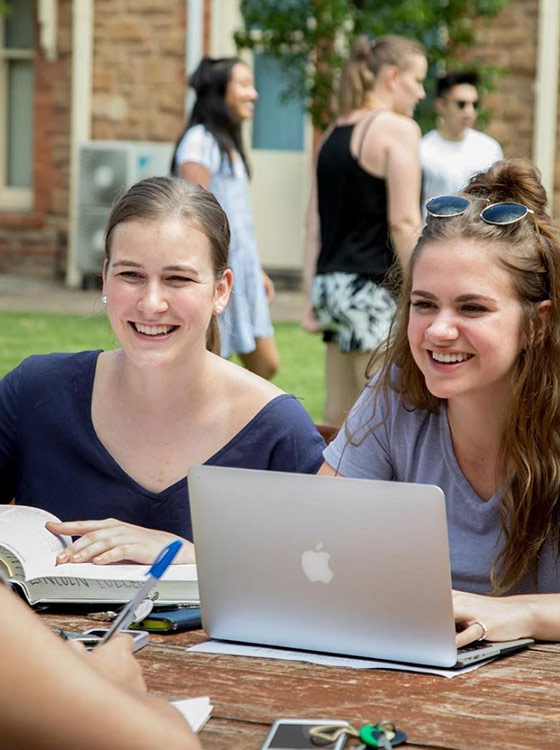 College students, happy and working with a book and laptop outdoors.
